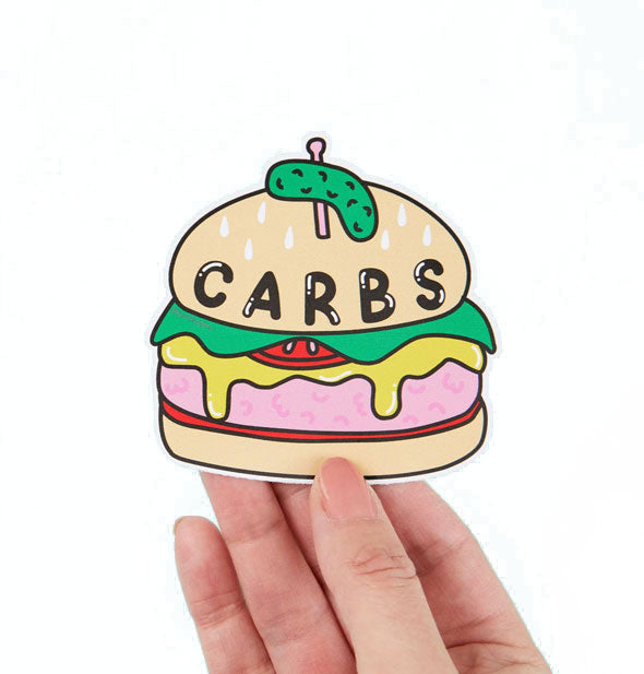 Model's hand holds a sticker designed to look like a cheeseburger that says, "Carbs" on the bun in large bubble lettering