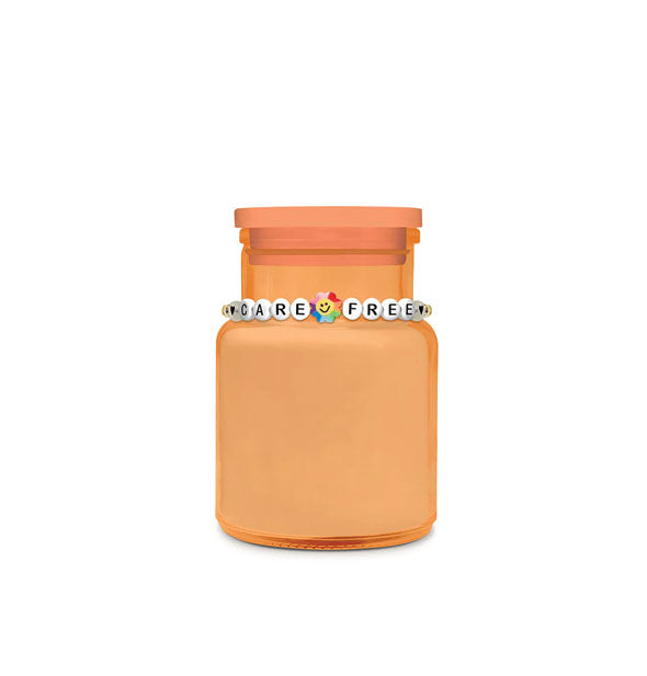 Orange glass jar candle with "Care Free" beaded bracelet around its neck
