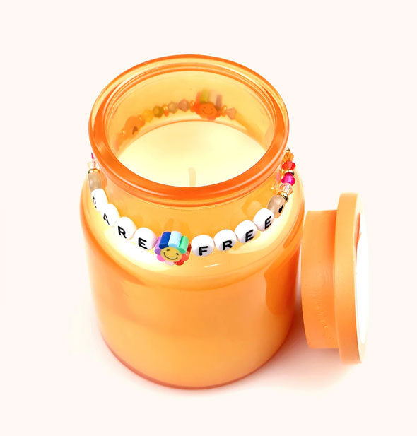 Opened orange glass jar candle with "Care Free" beaded bracelet around its neck