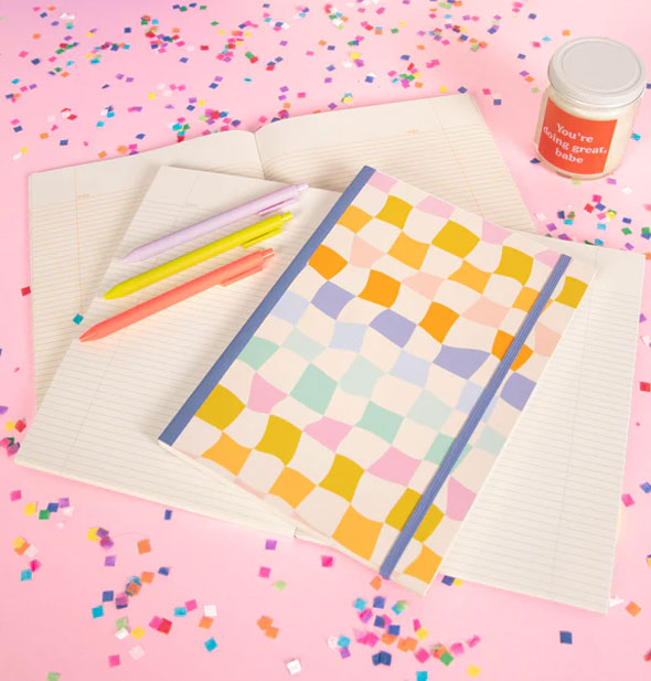 Carnival Checker Notebooks and pens on a pink surface scattered with multicolored confetti 