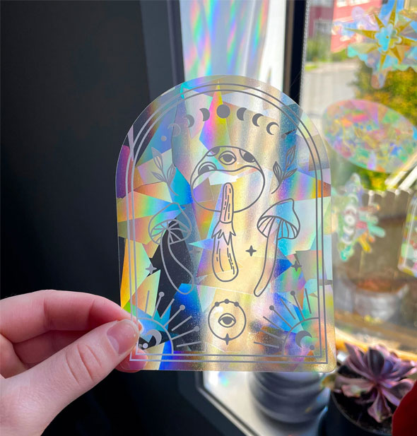 Model holds a Celestial Mushroom Suncatcher Sticker in front of a window to demonstrate its prismatic effect