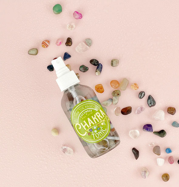 Bottle of Cucumber Chakra Tonic with multicolored gemstones inside the bottle and scattered alongside