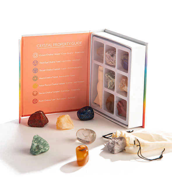 A collection of colorful stones sits in front of an upright, opened box containing more stones and a printed Crystal Property Guide.