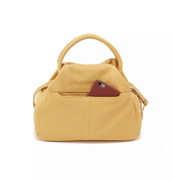 Opposite side of pale yellow leather bag shows an exterior phone slip pocket with phone partially emerging from it