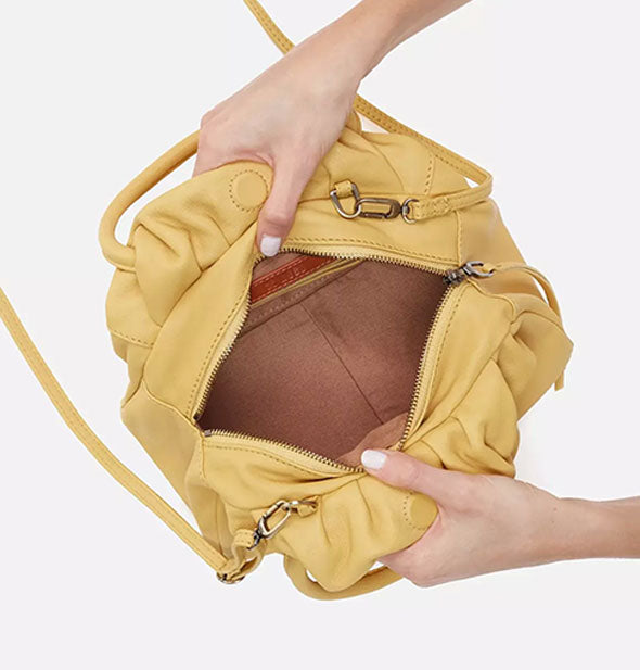 Model's hands hold open a pale yellow leather purse to reveal its tan lining