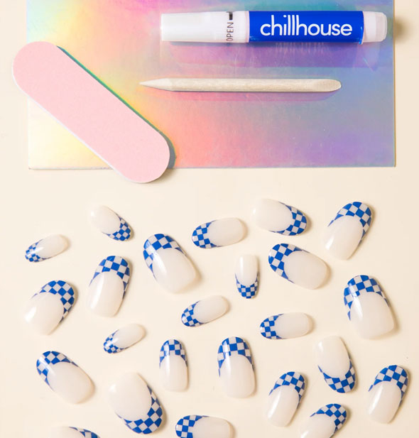 Contents of the Chillhouse press-on nail kit: Blue checker print tipped nails in a variety of sizes, small pink file, wooden cuticle pusher, and glue tube