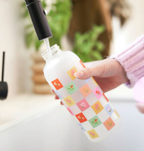 Model fills a Checkerboard Blooms Glass Water Bottle with tap water
