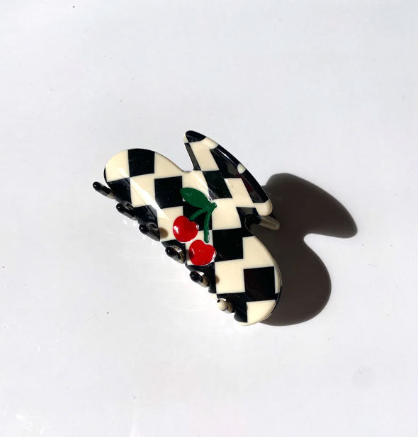 Black and white checkered claw clip featuring a small central design of red cherries with green stems and leaf