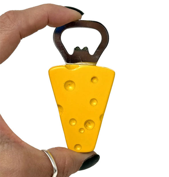 Model's hand holds a Swiss cheese wedge bottle opener between thumb and index finger for size reference