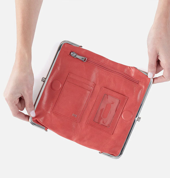 Model's hands hold open a salmon-colored leather wallet with silver hardware and numerous storage pockets