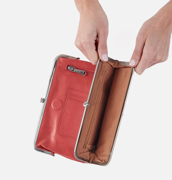 Model's hands hold open a salmon-colored leather wallet compartment with brown lining and silver frame hardware