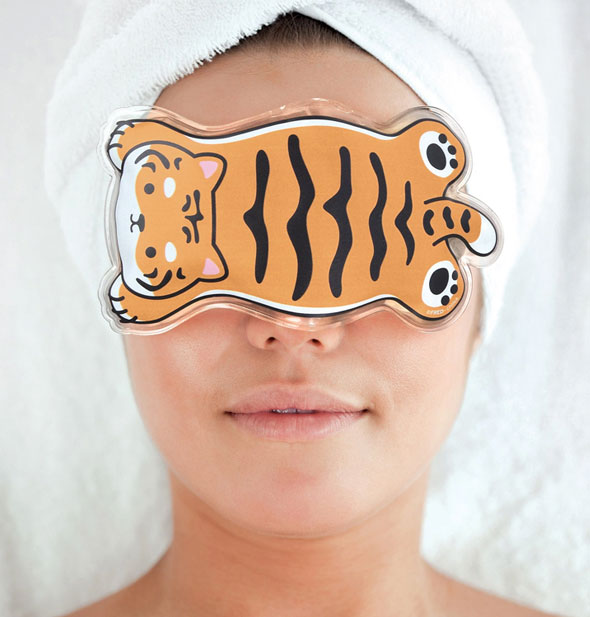 Model with hair wrapped up in a white towel wears a cartoon tiger gel mask over eyes