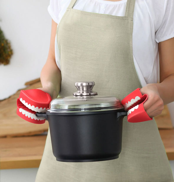 Model wears Chomp "chattering teeth" style potholders on hands to carry a crock by the handles
