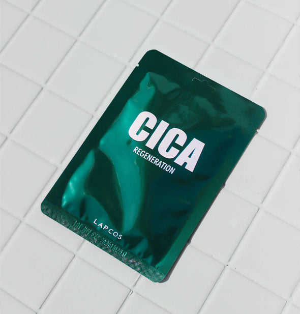 Dark green metallic packet of Lapcos Cica Regeneration sheet mask rests on a white tiled surface