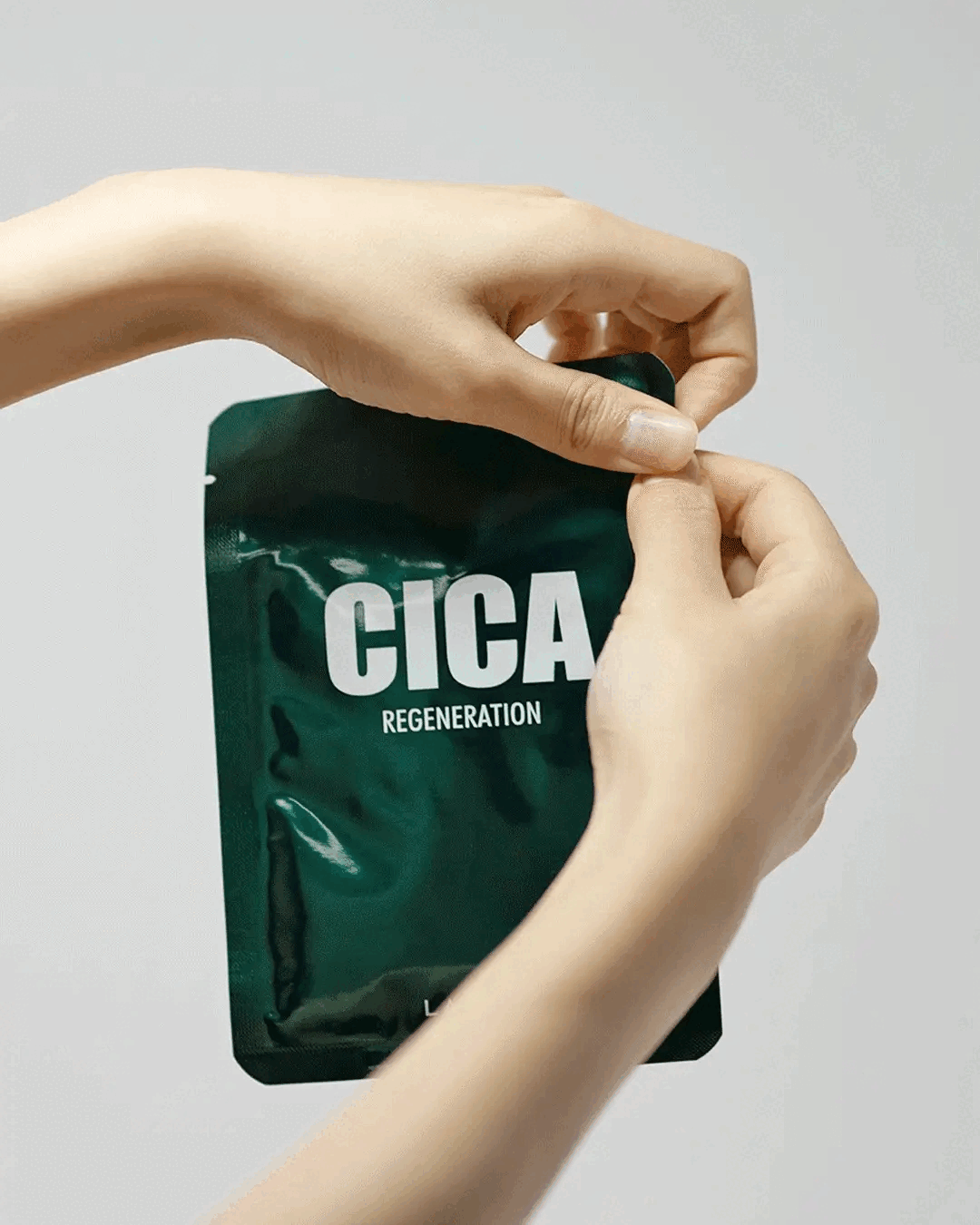 Model removes a Cica Regeneration sheet mask from dark green packet and unfolds it