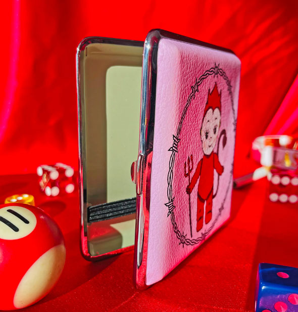 Devil Kewpie doll cigarette case shown standing on end and slightly open to reveal green interior with black elastic band