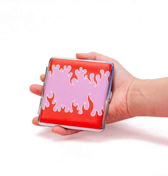 Model's hand holds a square cigarette case with pink and red flame design and silver edge