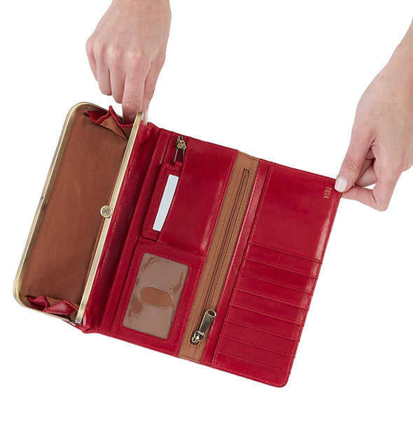 Model's hands hold open a red leather wallet with brown lining and brass hardware