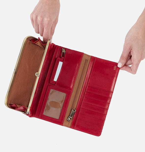 Model's hands hold open a red leather wallet with brown lining and brass hardware