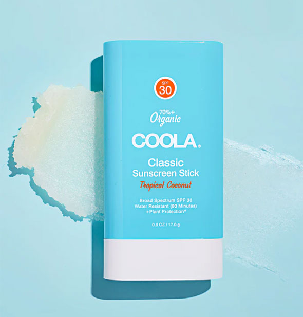 A tube of Coola Classic Sunscreen Stick rests on top of a thickly smeared application of product