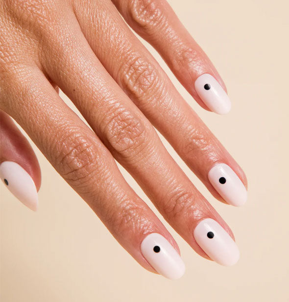 Model's hand wears a set of white press-on nails each with a single black dot