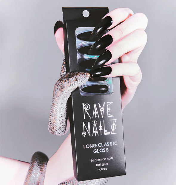 Model's hand wearing long black stiletto nails grasps a pack of Long Classic Gloss Rave Nailz with a snake wrapped around it