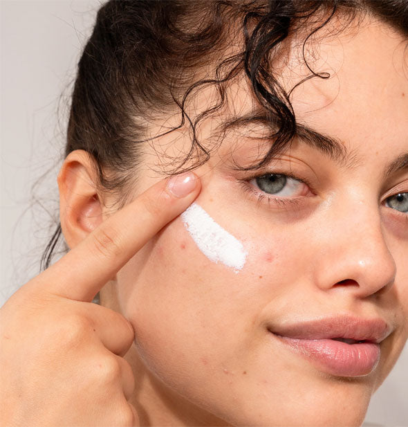 Model applies a streak of white sunscreen moisturizer to cheek