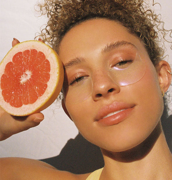 Model holding half a grapefruit wears eye patches under eyes