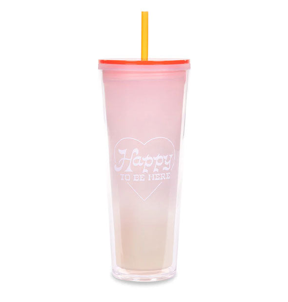 Light pink drink tumbler with yellow straw says, "Happy to be here" in white lettering inside a white heart outline