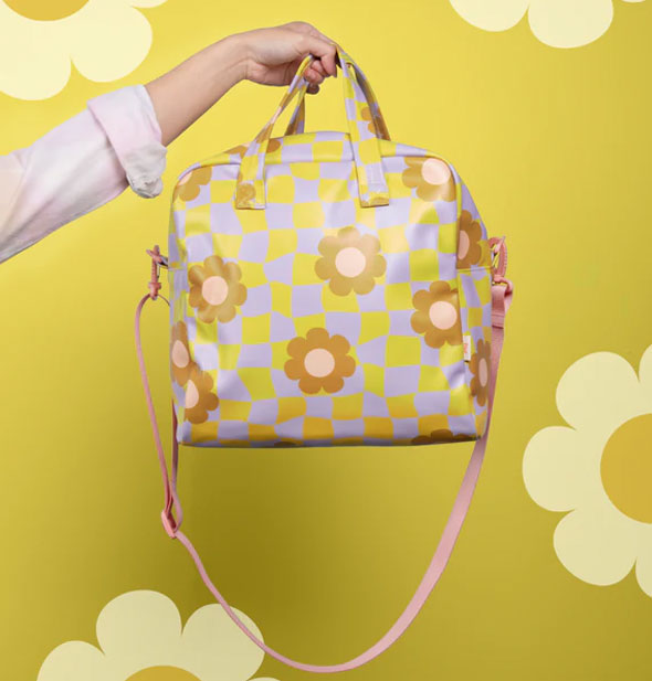 Model's outstretched hand holds the top straps of a Cool Funky Daisy Skate Bag against a lime green daisy print backdrop