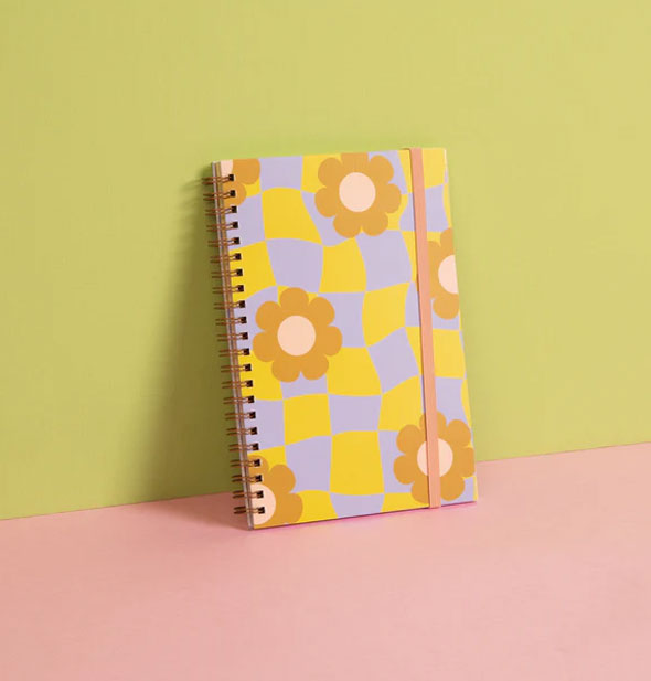 Cool Funky Daisy Spiral Notebook is set on end leaning against a green backdrop