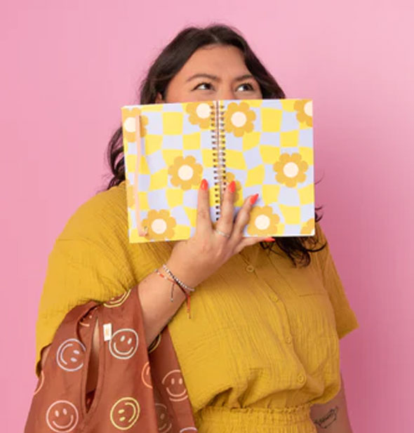 Model holds an opened Cool Funky Daisy Spiral Notebook in front of face