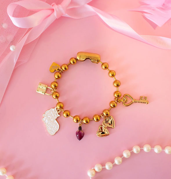 Chunky gold ball chain charm bracelet with gold heart, gold padlock, white enamel cat, purple rosebud, gold locket hearts, and gold key charms attached