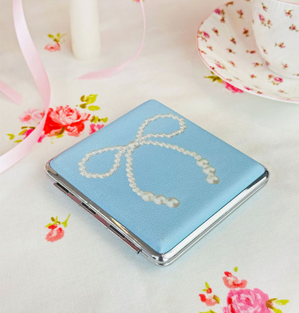 Rectangular blue cigarette case with white cat graphic and silver frame on a floral-patterned surface