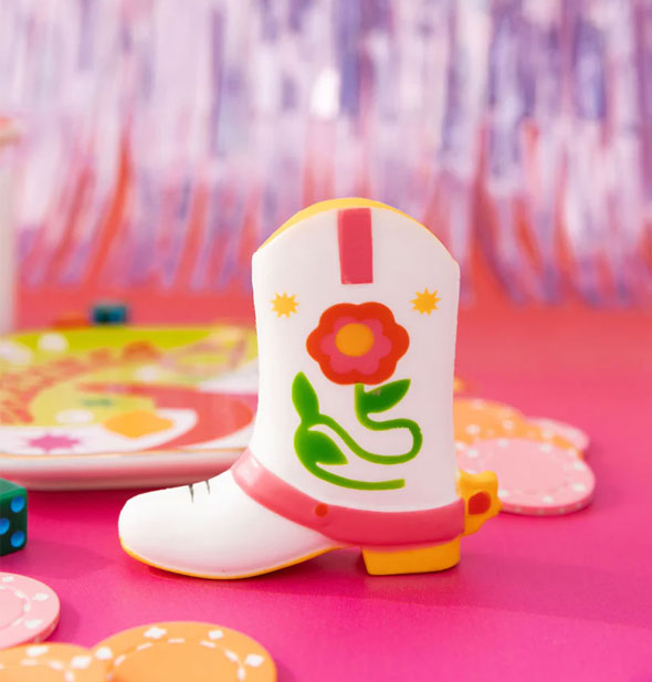 White, yellow, pink, red and green foam cowboy boot on a pink tabletop with poker chips