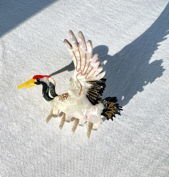 Crane claw clip with quartz-effect white body, black details accented with gold, a red head, and yellow beak rests on light wash denim