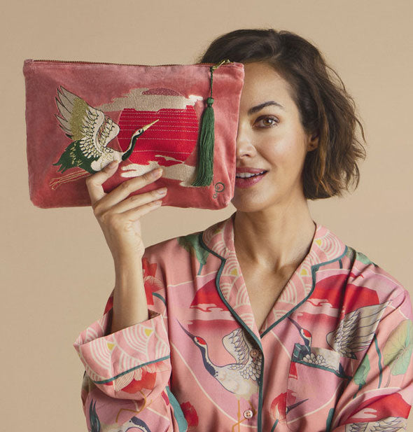 Model holds a pink velvet crane pouch in front of one eye