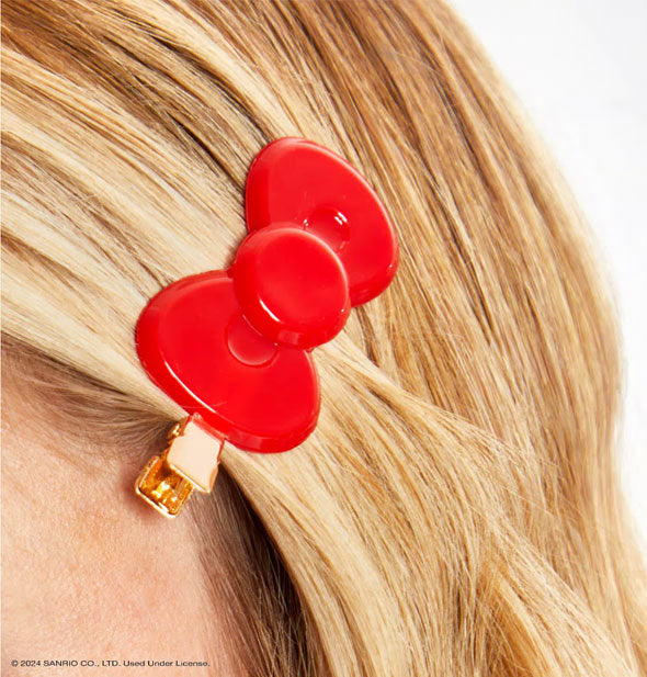 Model wears a red bow-shaped clip with gold hardware to secure bangs at temple