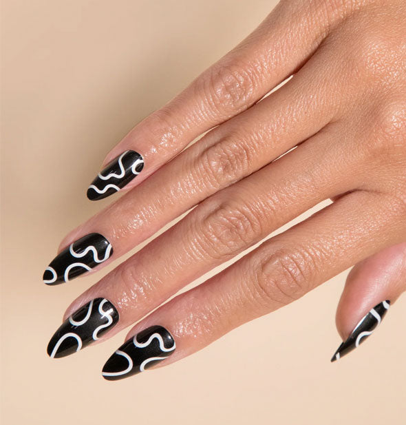 Model's hand wears press-on nails featuring a black base with abstract white wavy lines design
