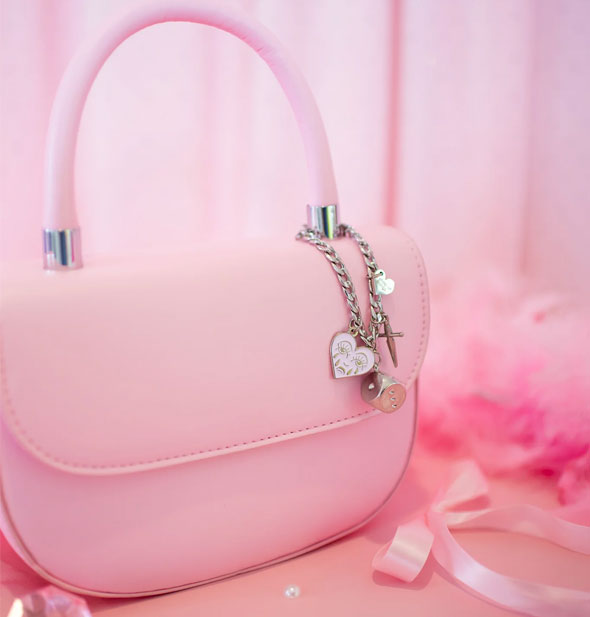 Silver charm chain hangs from the handle of a pink handbag on a surface with other pink items