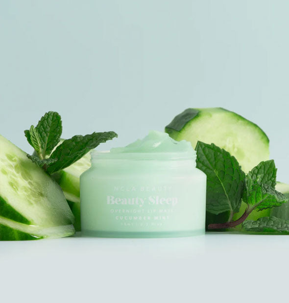 Opened pot of Cucumber Mint NCLA Beauty brand Beauty Sleep Overnight Lip Mask staged with slices of cucumber and sprigs of minr