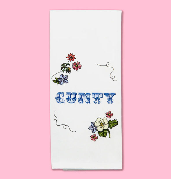 White dish towel with floral illustrations and flourishes says, "Cunty" in decorative blue lettering