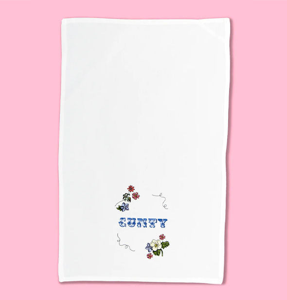 White dish towel with floral illustrations and flourishes says, "Cunty" in decorative blue lettering