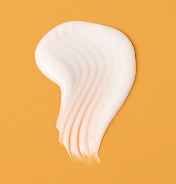 Closeup of a dollop of Verb Curl Leave-In Conditioner with streaks raked through it on an orange surface