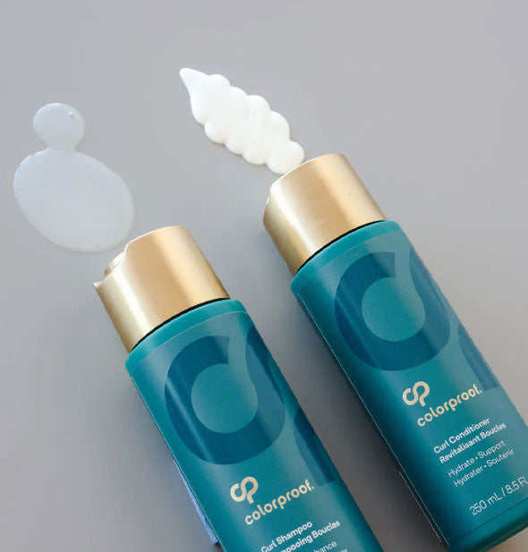 Bottles of ColorProof Curl Shampoo and Curl Conditioner laid on their sides dispense product onto a gray surface