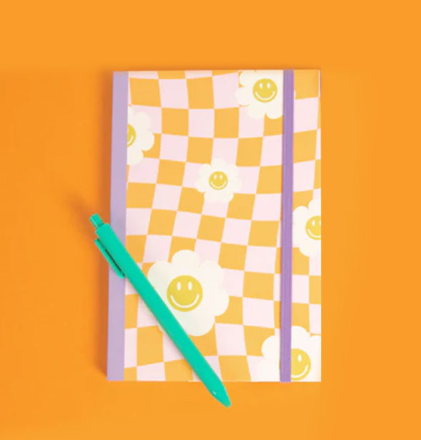 Daisy Checker Gratitude Journal rests on an orange surface with a sea green pen