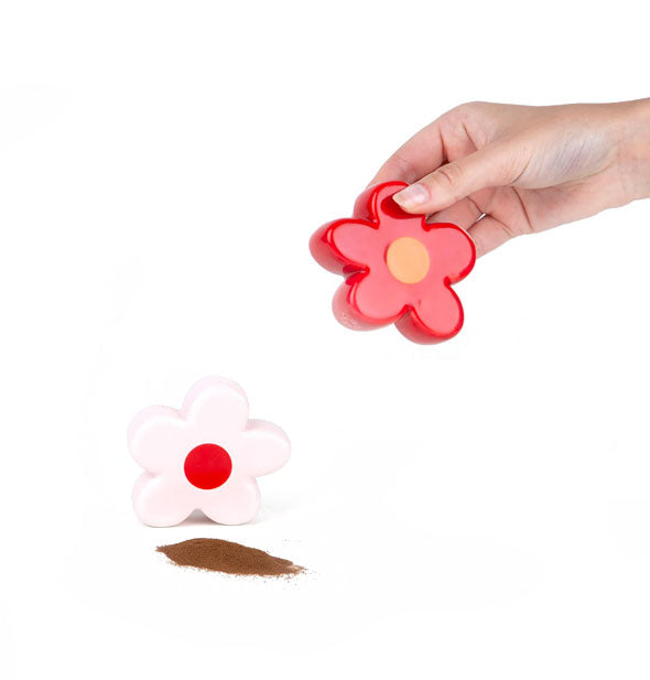 Model holds a red daisy shaker near a pink daisy shaker with a brown spice pile in front of it