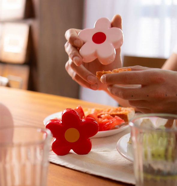 Model seated at a table with plates of food and glassware uses a set of red and pink daisy salt and pepper shakers
