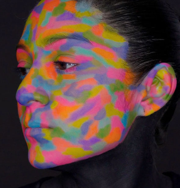 Model's face is fully covered in colorful DayGlo paint streaks