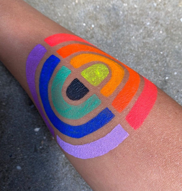 Model's arm is painted with mirrored rainbows in stripes of purple, blue, teal, orange, red-orange, and neon coral surrounding black and yellow half-circles